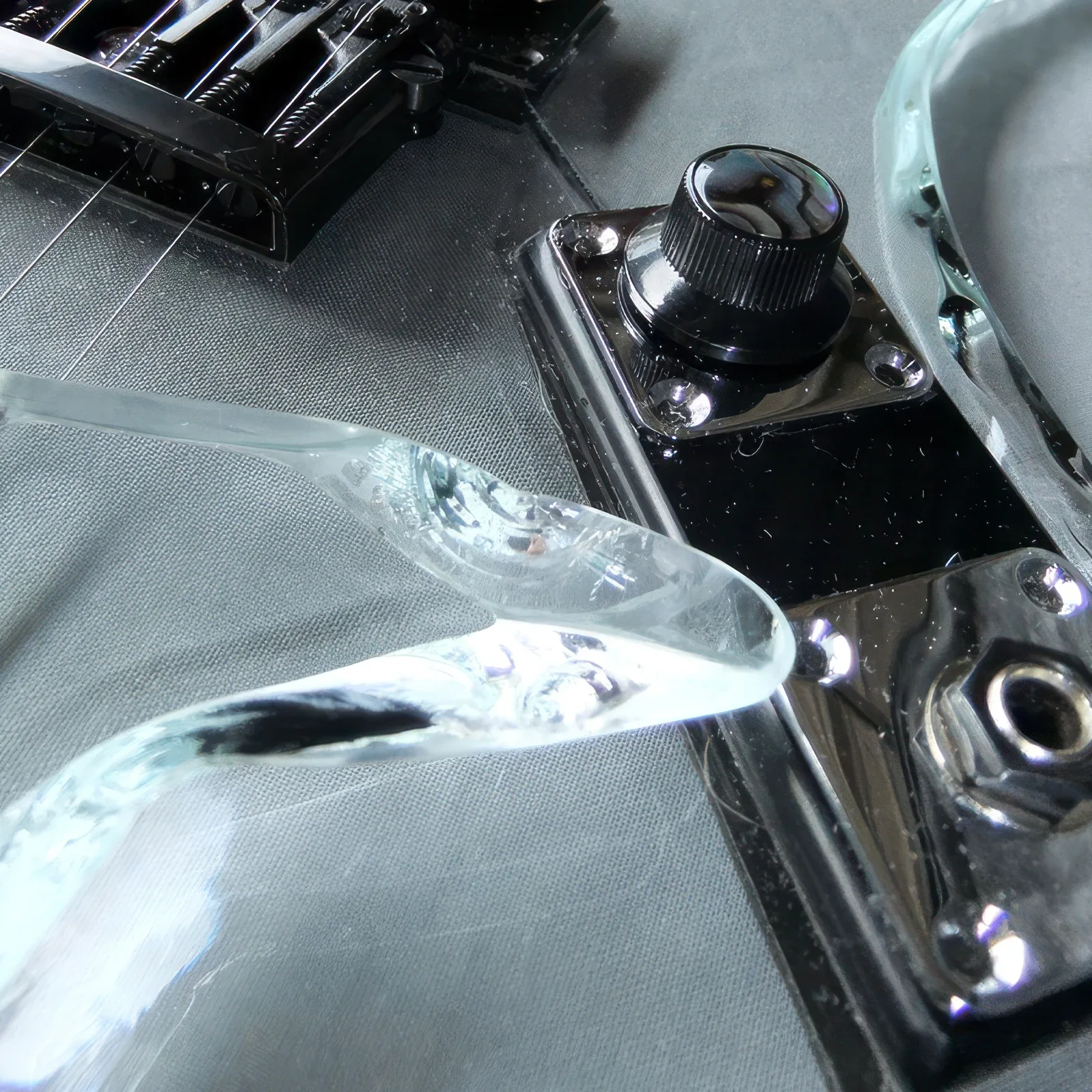 close up of black guitar control knob jack plate and clear glass body edge